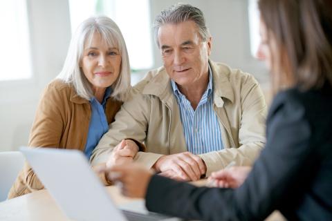 A retiree couple in a meeting with a professional. They are all looking at a laptop screen